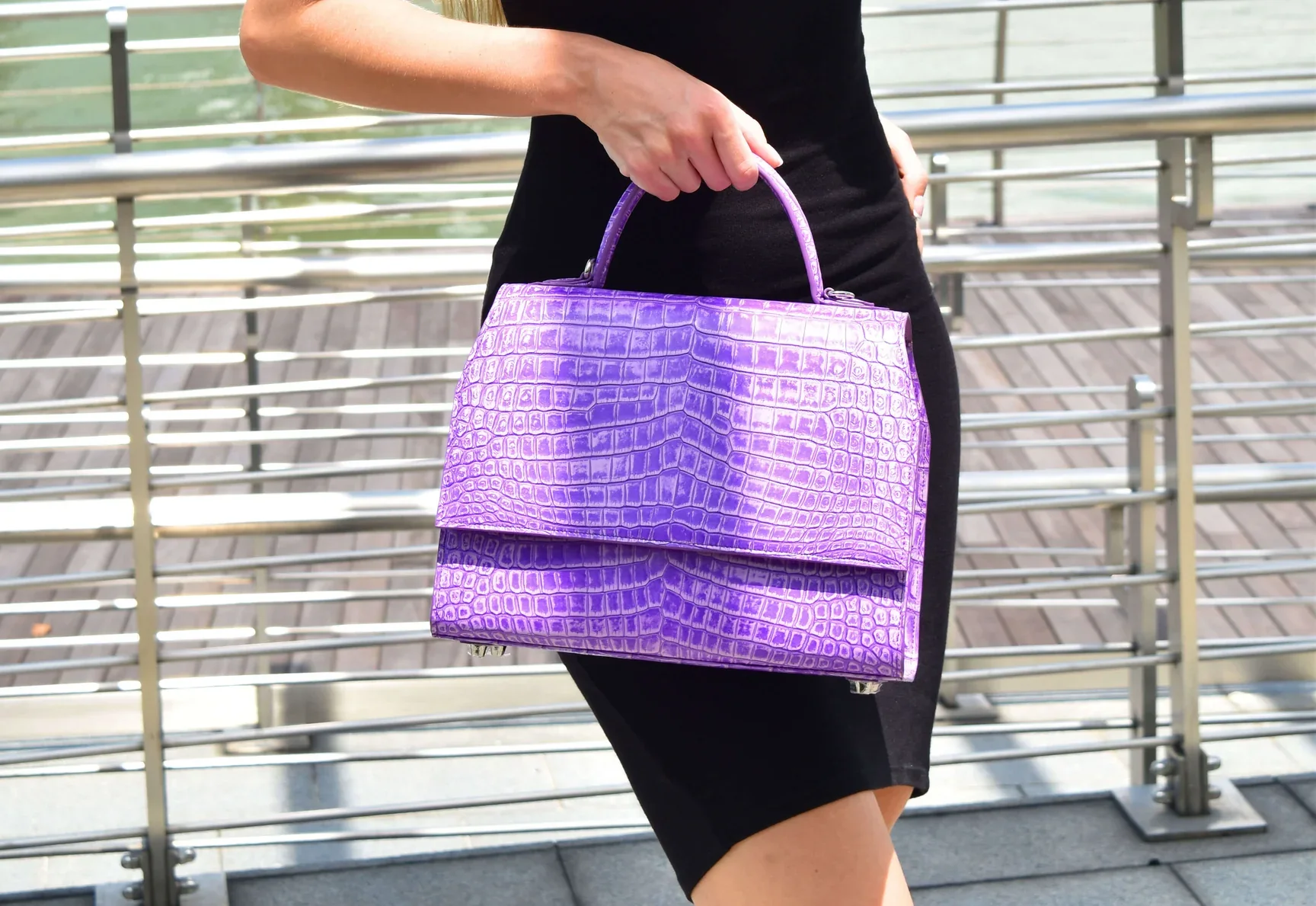 Violet Nilo top-handle bag with a marbled finish, carried by hand beside the marina
